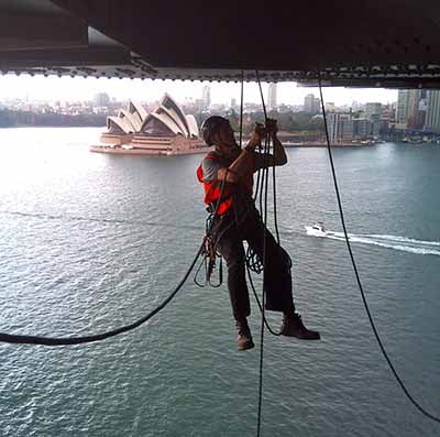 Rope access worker suspended under a bridge near the opera house in Sydney, Australia