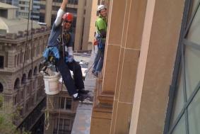 Two workers hanging on ropes outside of building to reach windows 