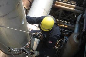 Employee in Petrochemical industry climbing on pipe to check measurements