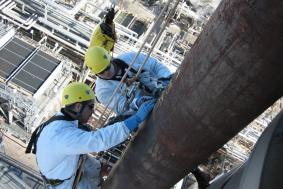 Two employees using rope access to reach high spot on pipeline refinery