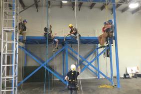 Five students on blue scaffold working on rope access training with technician observing