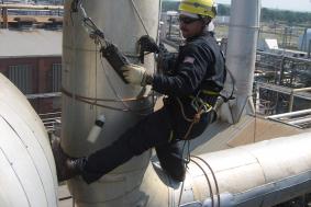 Employee in Oil & Gas industry using rope access at pipeline refinery to check measurements